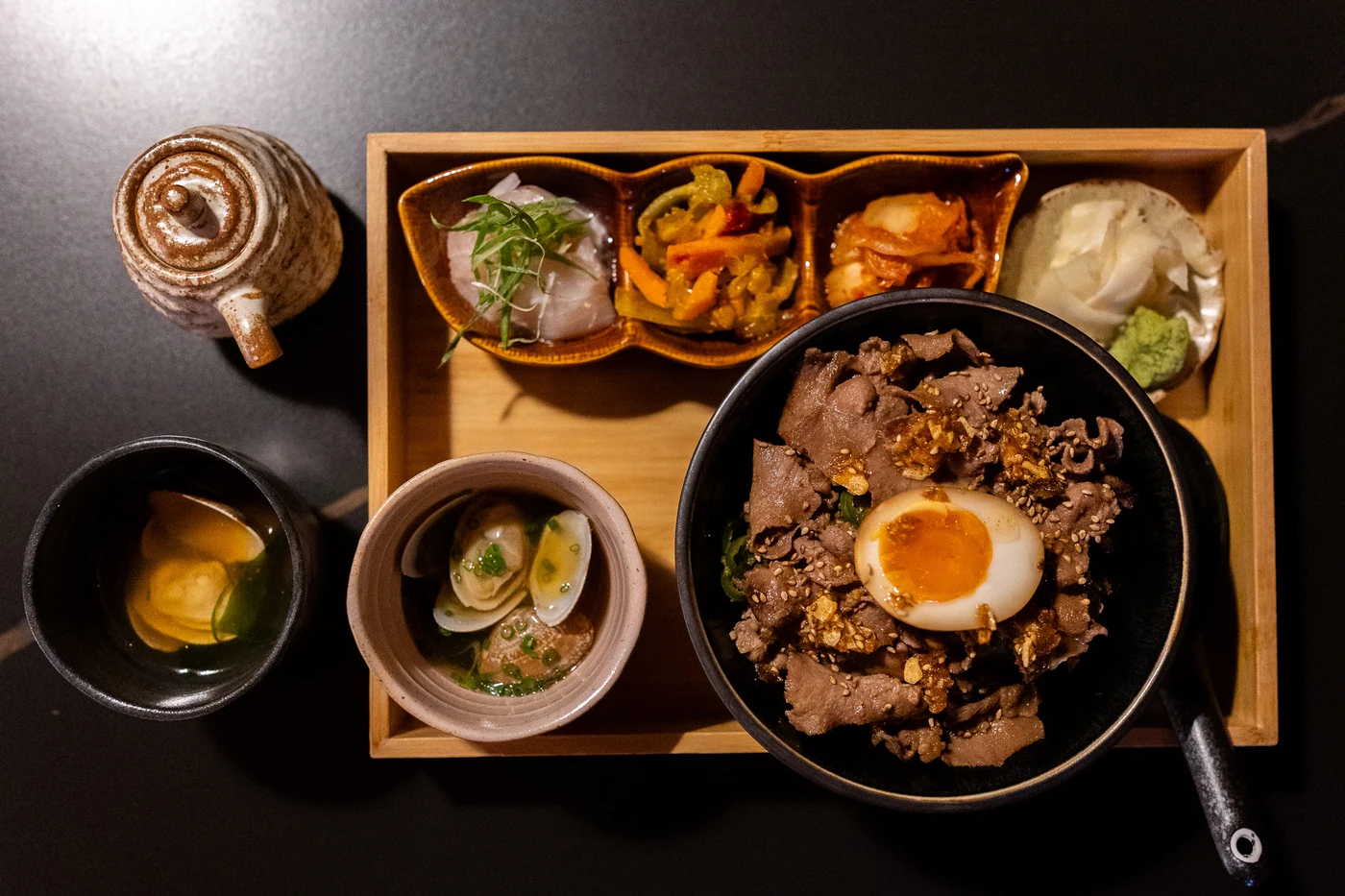 A meat and rice bowl with egg and side dishes at Jaya